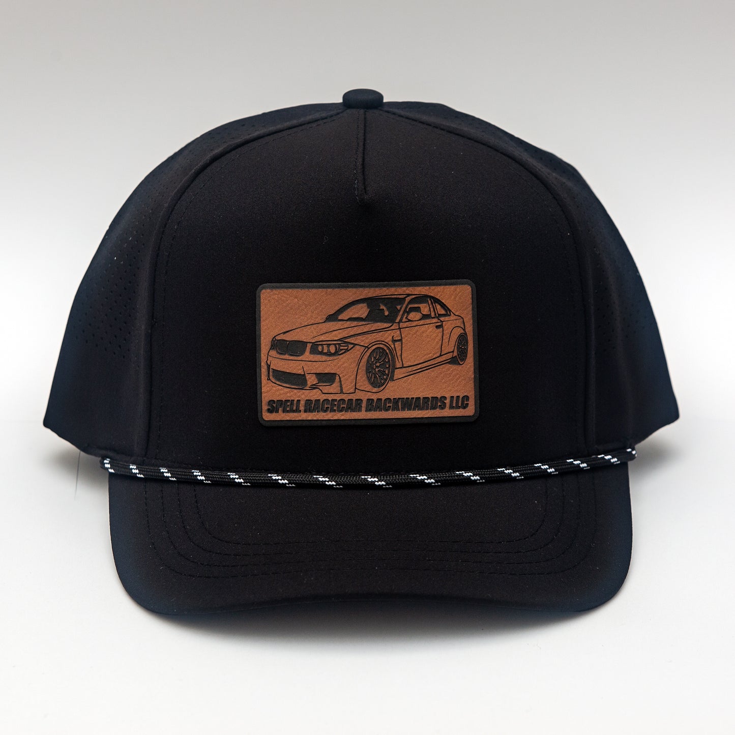 front view of black ball cap with leather patch with illustration of car, photographed on white background